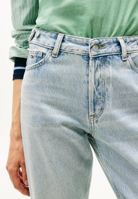 Jeans de mezclilla azul claro con cintura alta, botón plateado y costuras amarillas. Cuenta con bolsillos y un diseño ajustado.