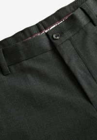 Pantalones de tela negra con textura y corte plano, que cuentan con cierre de botón y un forro de cinturilla lisa en un patrón púrpura contrastante.