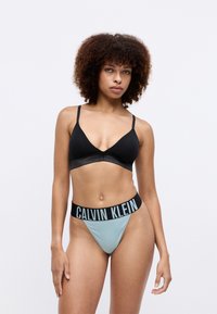 Zwarte bralette met dunne bandjes en een logoband. Mintgroene string met een zwarte elastische tailleband met 'CALVIN KLEIN' in vetgedrukte letters.