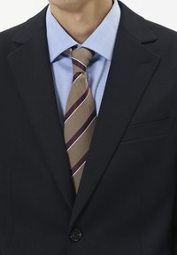 Férfi világoskék inget, sötétkék textúrájú zakót és barna csíkos nyakkendőt visel, amely elöl be van gombolva.