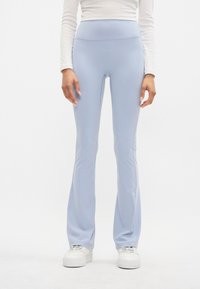 Leggings a campana di un blu chiaro realizzati in tessuto elasticizzato e liscio. Presentano una vita alta e sono abbinati a sneakers bianche.