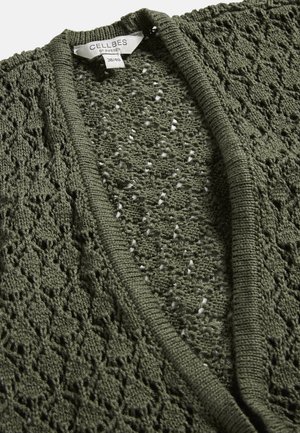 Close-up af olivengrøn strikket cardigan med diamantmønster og synligt mærke "Cellbes of Sweden" i størrelse 38/40.