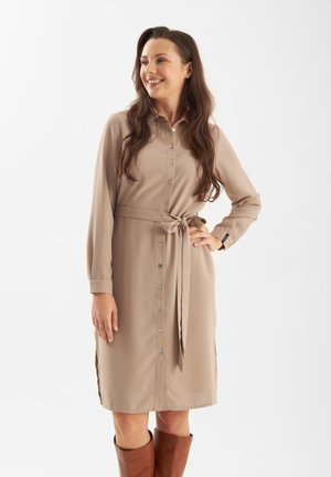 Beige Hemdkleid mit Kragen, langen Ärmeln, gebundenem Taillenbund und seitlichen Schlitzen, kombiniert mit knallhohen braunen Stiefeln. Glatte Stofftextur.