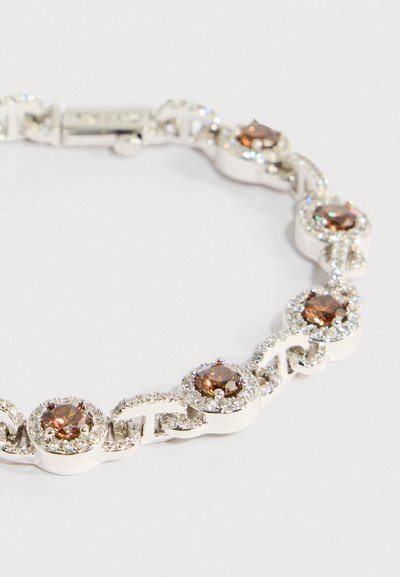 Ezüst karkötő kerek barna drágakövekkel, amelyeket apró, tiszta kristályok vesznek körbe, biztonságos kapoccsal, fehér háttéren.