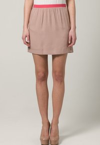 Falda con cinturilla rosa y tela de color beige claro, de textura suave, corte recto y diseño de altura media, combinada con tacones nude.