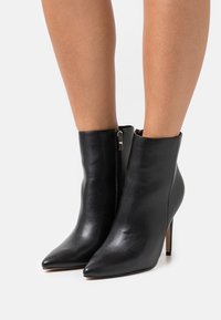 Stivaletti in pelle nera con punta affilata e tacco a stiletto. Presentano un design elegante e una chiusura con zip laterale.