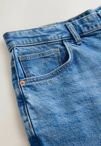 Niebieskie dżinsy z denimu z wyblakłą fakturą, posiadające standardową talię, przednią kieszeń i widoczne miedziane nity.