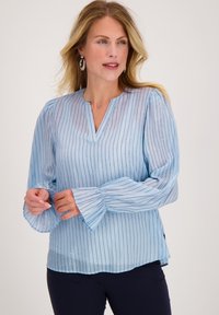 Lichtblauwe blouse met verticale strepen, lange puffmouwen en een V-hals. De stof heeft een subtiele glans met kleine decoratieve accenten.