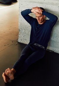 Navy long-sleeve shirt and fitted leggings, both made of soft material, worn by a seated figure against a concrete wall.