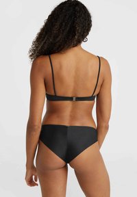 Completo bikini nero con spalline sottili e un design semplice, caratterizzato da una chiusura sul retro e una texture liscia.