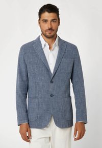 Mėlynas tekstūruotas �švarkas su dviem priekinėmis kišenėmis, iškirptėmis atvartais ir dviem mygtukais, dėvimas ant baltos marškinės. Priderintas siluetas moderniam stiliui.