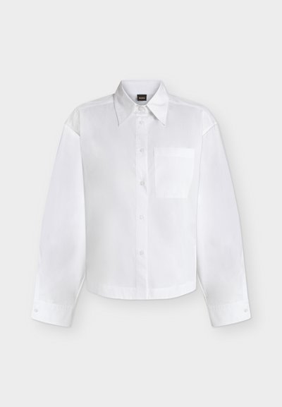 Chemise blanche à manches longues boutonnée, avec col pointu et poche poitrine, présentée sur un fond clair uni.