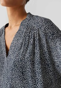 Blusa a righe blu navy e panna con scollatura a V e dettagli plissettati. Tessuto morbido con un design astratto di forme e texture irregolari.