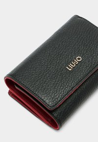 Czarny portfel ze skórzanym teksturowanym wykończeniem, z czerwonym wnętrzem. Charakteryzuje się złotym logo i kontrastowym przeszyciem, z złożonym projektem. Kompaktowy i elegancki.