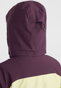 Kapuzejacke mit einem dunkelvioletten oberen Bereich und einem hellgelben unteren Bereich. Verstellbare Kapuze mit Kordelzug. Glatte Oberfläche.