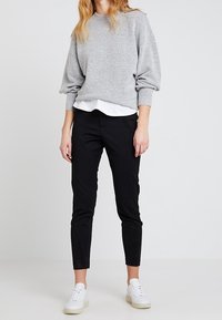 Maglione pullover grigio chiaro con maniche a palloncino sopra una camicia bianca con colletto, abbinato a pantaloni neri aderenti e sneakers bianche.