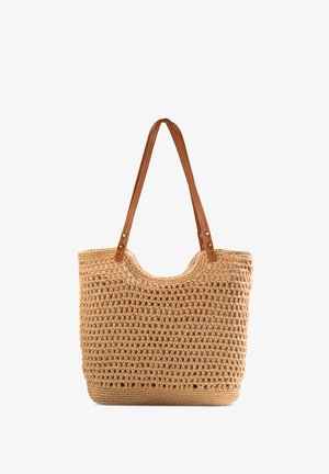 Beżowa torba na zakupy z szydełka z brązowymi skórzanymi uchwytami, teksturowanym korpusem, otwartą górą i okrągłym kształtem. Zauważalny wzór tkany w całej torbie.