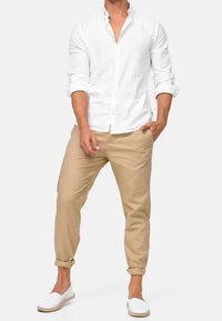 Camicia bianca in lino con bottoni, pantaloni beige a gamba affusolata e espadrillas bianche. Maniche risvoltate e pantaloni con risvolto. Design semplice e casual.