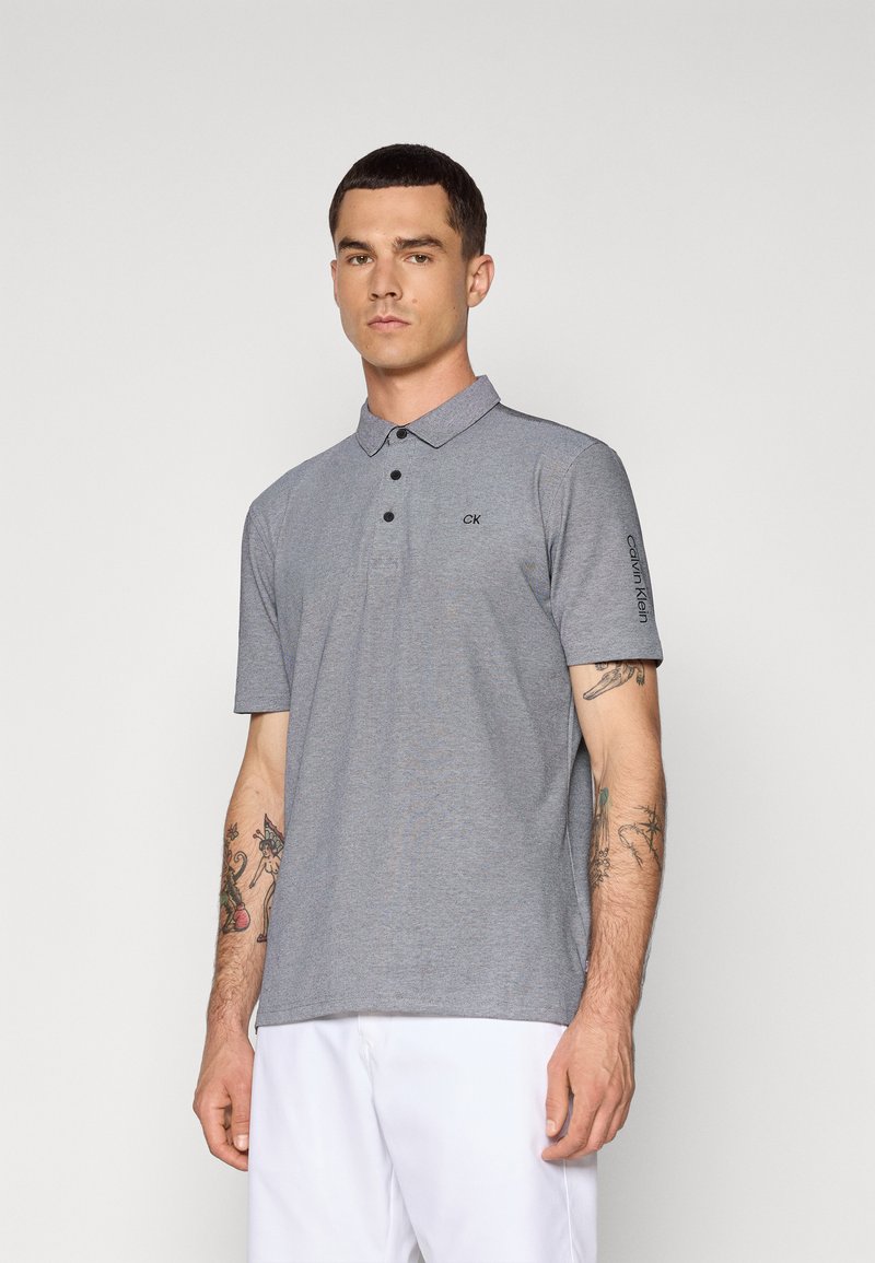 Camisa polo cinza com um design de colarinho, mangas curtas e três botões pretos. Apresenta um logótipo subtil no peito e detalhes nas mangas.