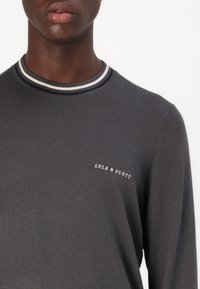 Sivi pleteni pulover s okruglim ovratnikom koji ima prugasti rebrasti dekolte. Logo branda "LYLE & SCOTT" otisnut u bijeloj boji blizu prsnog dijela.