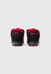 Black and red sneakers with padded collar and tongue, featuring "GLOBE" logo on heel and contrasting red accents on a black base.