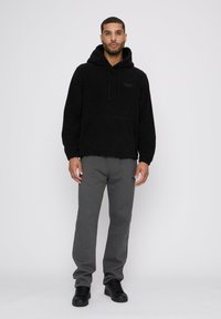Schwarzer Fleece-Hoodie mit einer Fronttasche und Kordelzug. Kombiniert mit grauen Sweatpants und schwarzen Sneakers, die einen lockeren Schnitt haben.