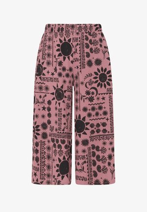 Różowe spodnie o szerokich nogawkach z czarnymi wzorami słońca, księżyca, gwiazd i kwiatów ułożonymi w dekoracyjne panele.
