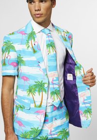 Costume bleu clair avec des motifs de flamants roses et de palmiers. Comprend des manches courtes, une cravate assortie et une doublure intérieure violette.