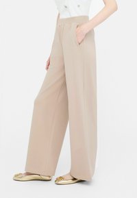 Pantaloni bej cu talie înaltă, croi larg, cu buzunare laterale și o textură netedă. Purtați cu pantofi plate aurii cu accente decorative.