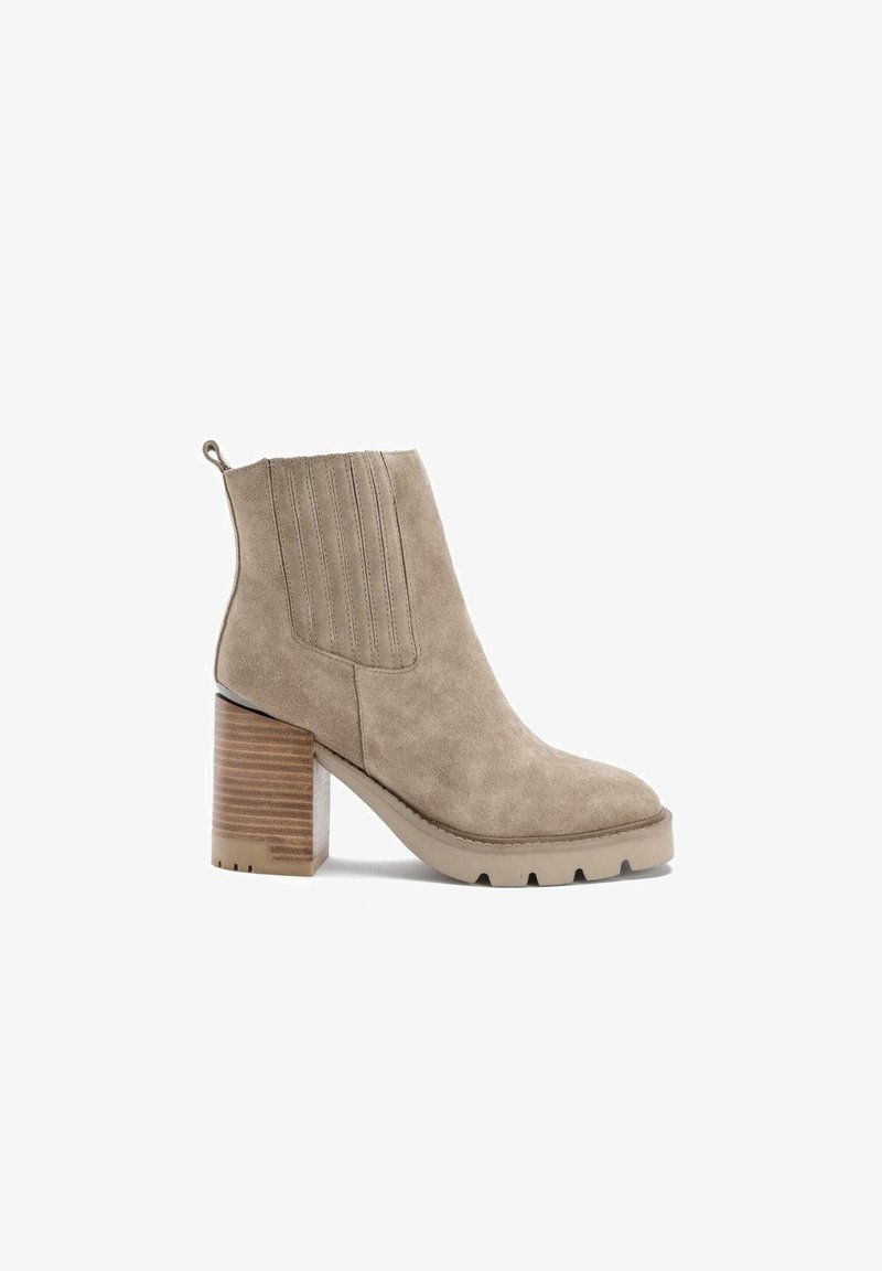 Bottine en daim beige avec talon épais empilé, panneau latéral élastique, patte de tirage et semelle en caoutchouc crantée.