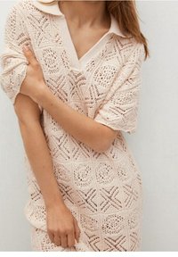 Robe-sweater en tricot oversize de couleur beige doux avec un col, mettant en avant des motifs géométriques et une texture en tricot ouvert.