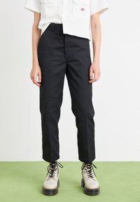 Sorte skreddersydde bukser med slim fit, med en glatt tekstur. Brukt sammen med kremfargede støvler og en kort hvit skjorte.