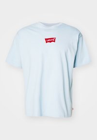 Světle modré bavlněné tričko s krátkým rukávem, kulatým výstřihem a červeným logem Levi's na přední straně. Hladká textura, volný střih a bez dalších vzorů.