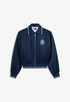 Marineblå zip-up jakke med hvit kant på krage, mansjetter og kant nederst, med et emblem på venstre bryst og to frontlommer.