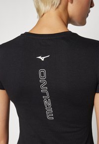 Juodas marškinėlis su prigludusia forma, su balta logo ir tekstu vertikaliai išdėstytais ant nugaros. Pagamintas iš minkštos, lygios medžiagos.