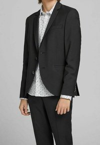 Černý saka s klopami, jednobotonovým zapínáním a bočními kapsami, kombinované s bílou košilí s černým abstraktním vzorem.