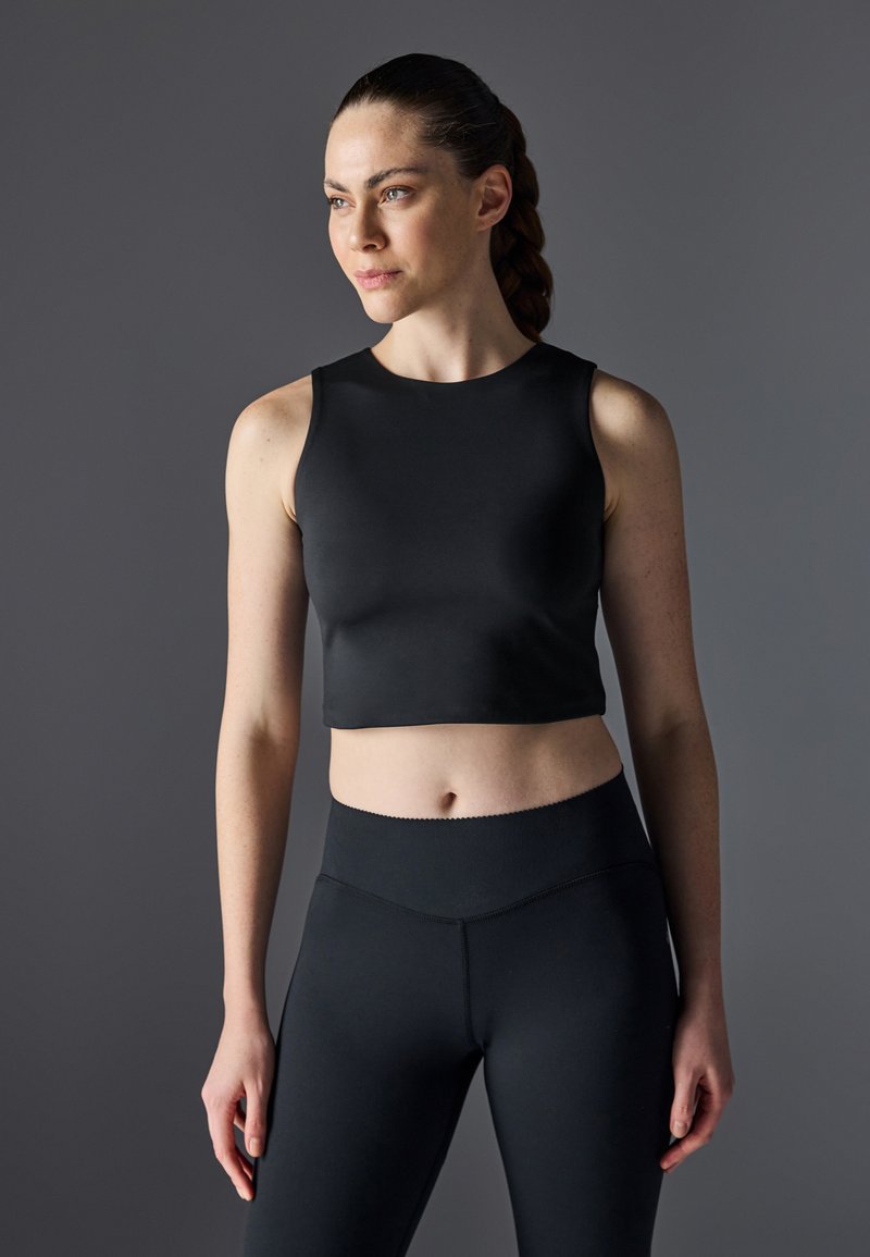 Top atlético negro corto hecho de tela suave, con un escote redondo y amplias sisas, combinado con leggings negros de cintura alta.
