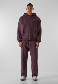 Haut à zip violet avec poches avant et pantalon assorti. Tissu doux, coupe décontractée, avec taille à cordon de serrage et logo sur la poitrine.