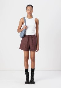 Haut sans manches blanc et shorts marron jusqu'à la taille. Bottes de combat noires, chaussettes noires et sac à épaule bleu clair. Design simple, look décontracté.