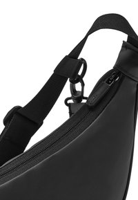 Čierna crossbody taška s nastaviteľným popruhom, otočným zapínaním a zipsom s označeným ťaháčikom na hladkom materiáli.