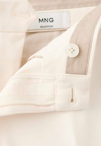 Camisa de botones beige con un patrón de espiga, que presenta un botón blanco, detalles en el collar en contraste y una etiqueta que dice "MNG SELECTION."