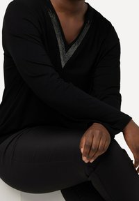 Czarny długi rękaw bluzka z dekoltem w serek i srebrnymi ćwiekami wzdłuż dekoltu, w zestawie z czarnymi obcisłymi spodniami. Miękki materiał, luźny krój.