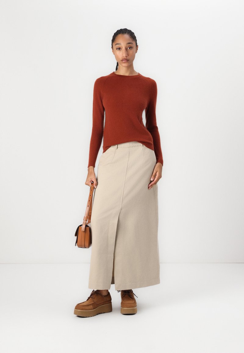 Rdzawoczerwony dopasowany sweter, beżowa maxi spódnica z bocznym rozcięciem, brązowe buty na platformie oraz mała brązowa torebka na ramię.