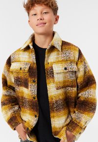 Gul- och brunrutigt flanellskjorta med knäppning fram, två bröstfickor och krage. Mjuk struktur med en lös passform.