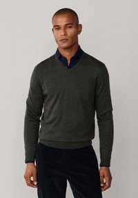 Donkergrijze v-hals trui van fijne gebreide wol, met een slim fit, geribbelde manchetten en zoom. Draagt over een marineblauw overhemd met kraag.