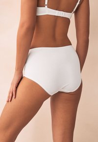 Culotte blanche en coton avec une texture lisse, présentant un bord festonné et une taille haute. Coutures plates sur un fond doux.
