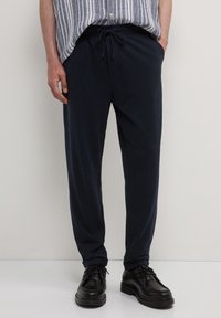 Marinefarbene Sweatpants aus weichem Stoff mit elastischem Bund, verstellbarem Kordelzug und Seitentaschen. Kombiniert mit schwarzen Schuhen.