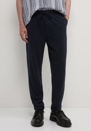 Marinefarbene Sweatpants aus weichem Stoff mit elastischem Bund, verstellbarem Kordelzug und Seitentaschen. Kombiniert mit schwarzen Schuhen.