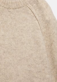 Bežový pletený sveter so zúženým okrúhlym výstrihom, mäkkou textúrou a mierne voľným tkaním. Viditeľné švy na pleciach.