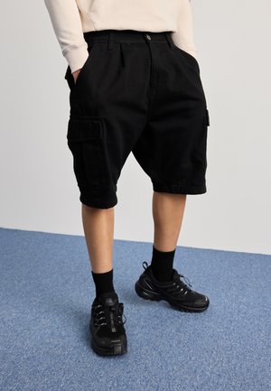 Shorts cargo noirs en coton, avec des poches latérales et une coupe droite. Associés à des baskets noires et des chaussettes mi-mollet.